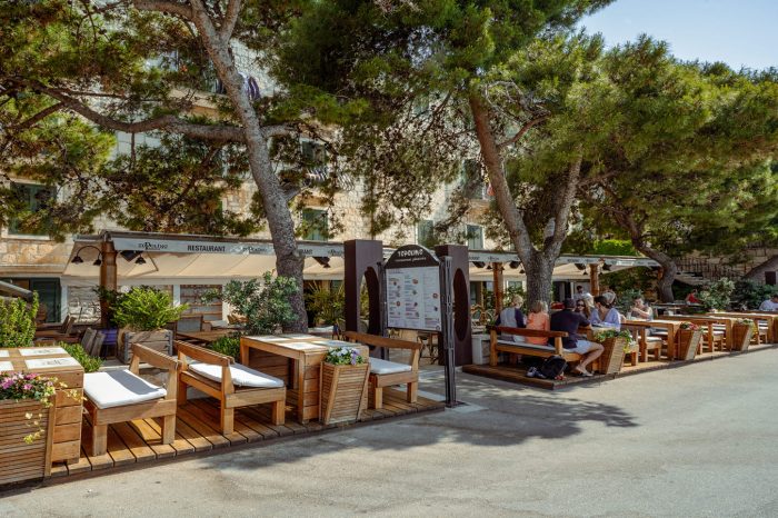 Gosti uživaju na drvenoj terasi restorana Topolino u hladu borova, uz opuštenu atmosferu i prirodno okruženje u centru Bola